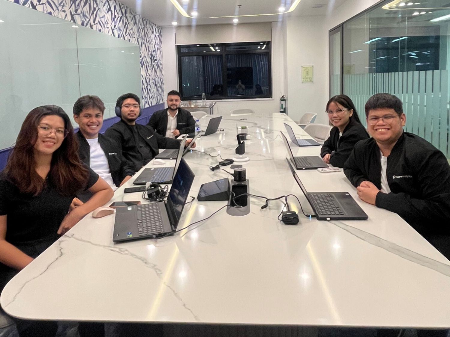 The FutureTeamsPH team smiling around the meeting room table with their laptops at the Manila office